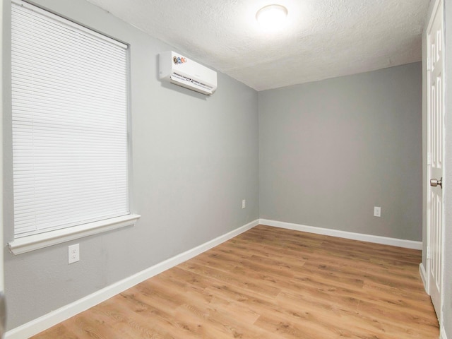 unfurnished room featuring a textured ceiling, light wood-type flooring, and a wall unit AC