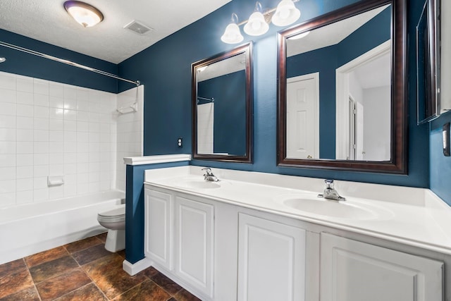 full bathroom featuring a textured ceiling, vanity, toilet, and tiled shower / bath