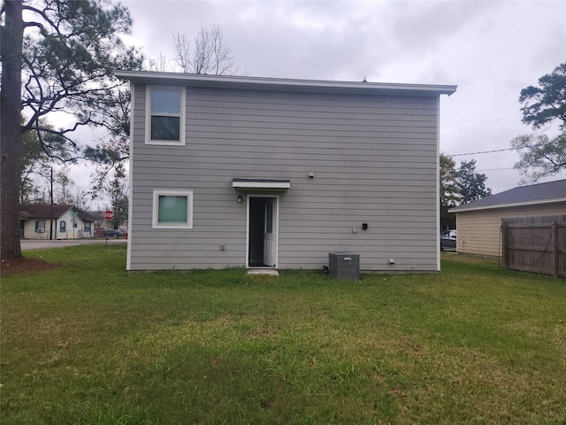 rear view of property featuring central air condition unit and a lawn