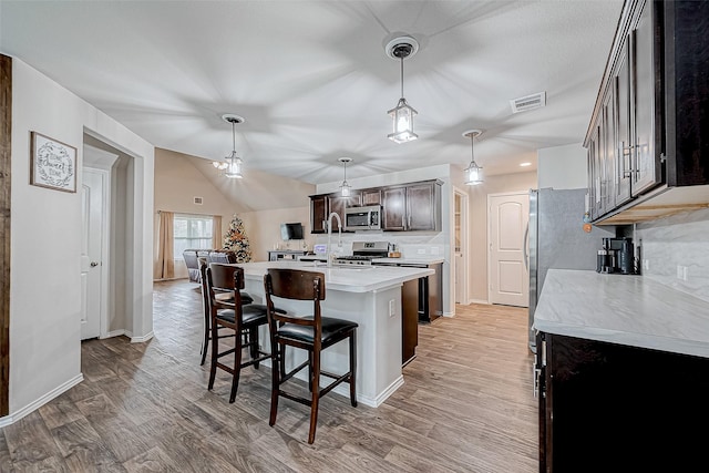 kitchen featuring dark brown cabinetry, stainless steel appliances, a center island with sink, light hardwood / wood-style flooring, and hanging light fixtures