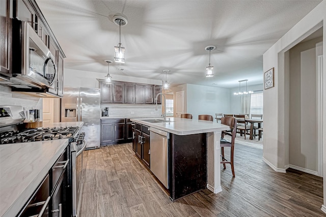 kitchen with a center island with sink, sink, appliances with stainless steel finishes, decorative light fixtures, and dark brown cabinetry