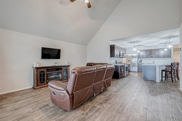 living room with ceiling fan, sink, lofted ceiling, and light wood-type flooring