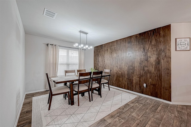 dining space with wood walls, light wood-type flooring, and a chandelier