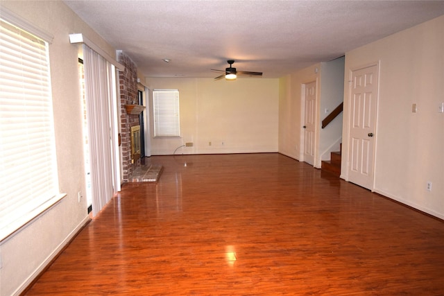 unfurnished room with a textured ceiling, ceiling fan, a fireplace, and dark wood-type flooring