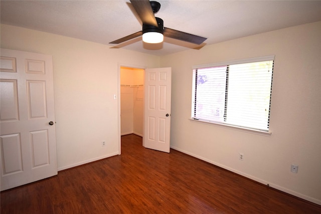 unfurnished bedroom with a spacious closet, a closet, ceiling fan, and dark hardwood / wood-style floors