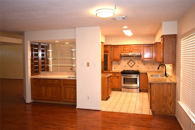 kitchen featuring decorative backsplash, sink, stainless steel range, and light hardwood / wood-style flooring