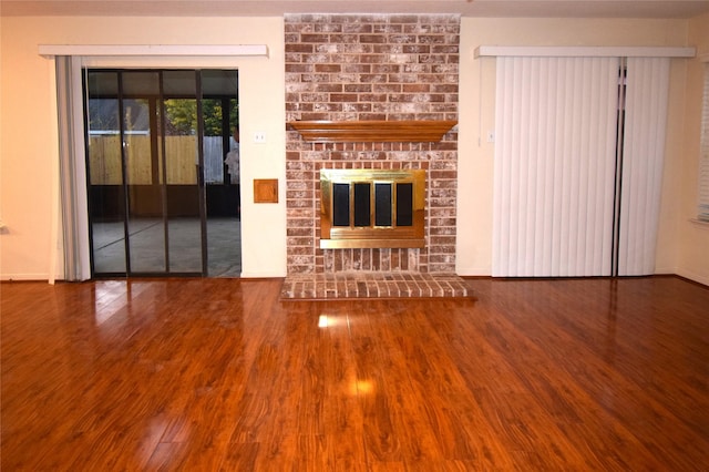 unfurnished living room with wood-type flooring and a brick fireplace