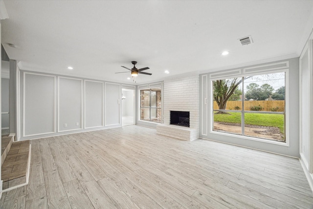 unfurnished living room featuring a fireplace, light hardwood / wood-style floors, ceiling fan, and crown molding