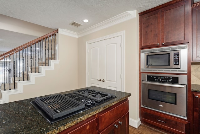 kitchen featuring dark stone counters, ornamental molding, a textured ceiling, appliances with stainless steel finishes, and dark hardwood / wood-style flooring