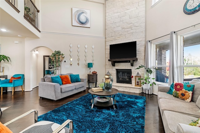 living room featuring a fireplace, a towering ceiling, a wealth of natural light, and dark wood-type flooring