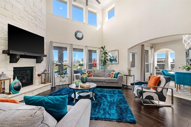 living room featuring a stone fireplace, a high ceiling, a wealth of natural light, and dark wood-type flooring