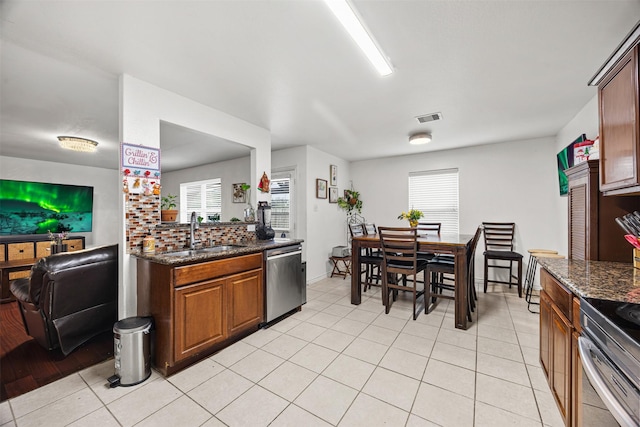 kitchen with backsplash, dark stone counters, sink, light tile patterned floors, and dishwasher