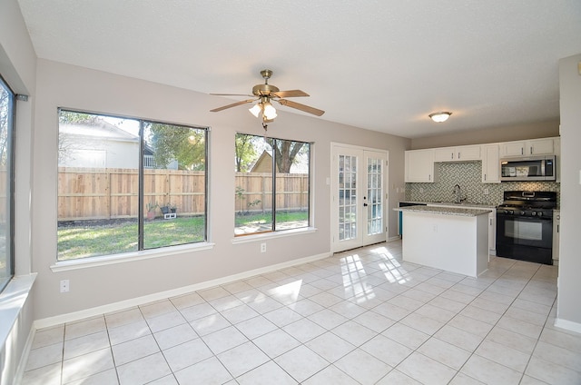 kitchen with decorative backsplash, black gas range oven, light tile patterned floors, white cabinets, and a center island