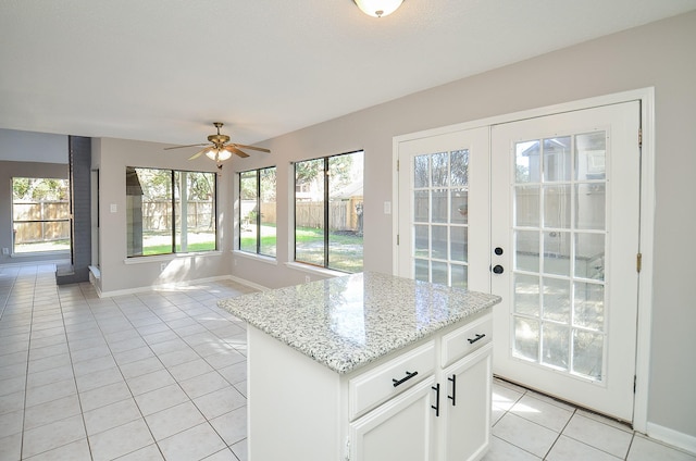 kitchen with a center island, white cabinets, ceiling fan, light stone countertops, and light tile patterned flooring