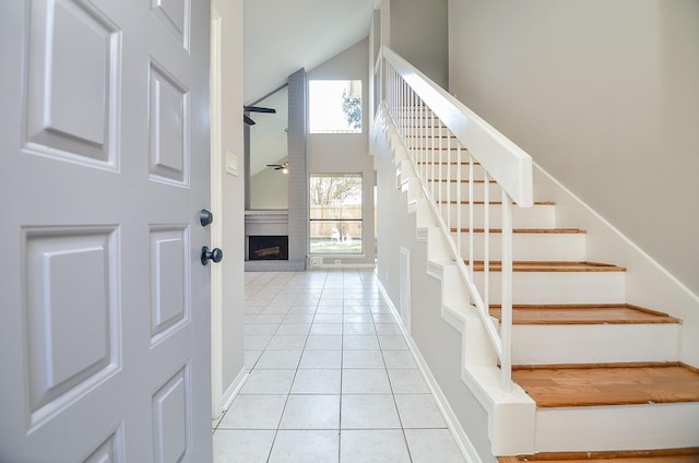 tiled entrance foyer featuring ceiling fan, a high ceiling, and a brick fireplace