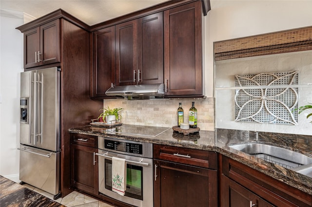 kitchen with decorative backsplash, dark brown cabinetry, stainless steel appliances, and dark stone countertops