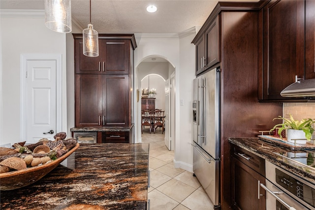 kitchen featuring appliances with stainless steel finishes, dark stone counters, ornamental molding, pendant lighting, and light tile patterned floors