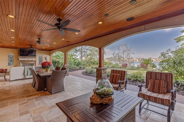 patio terrace at dusk featuring an outdoor stone fireplace and ceiling fan