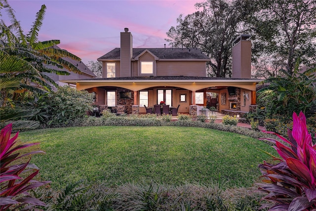 back house at dusk with a lawn and a fireplace