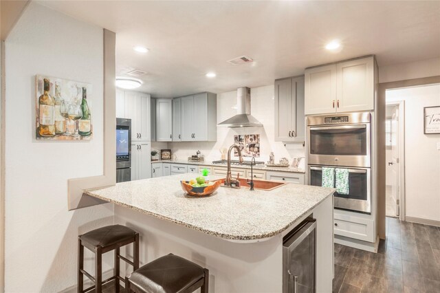 kitchen featuring light stone countertops, beverage cooler, visible vents, appliances with stainless steel finishes, and wall chimney range hood