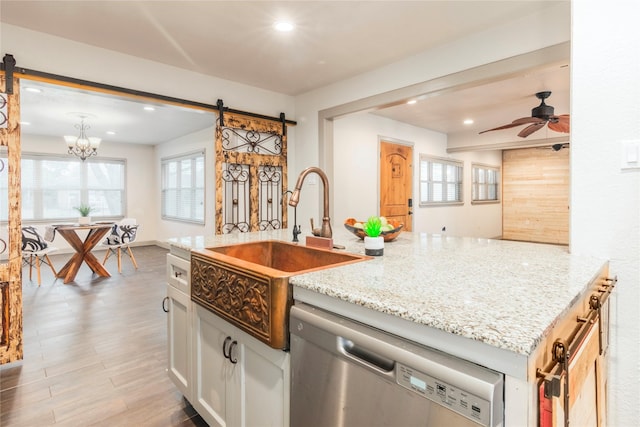 kitchen with sink, stainless steel dishwasher, a barn door, ceiling fan with notable chandelier, and white cabinets