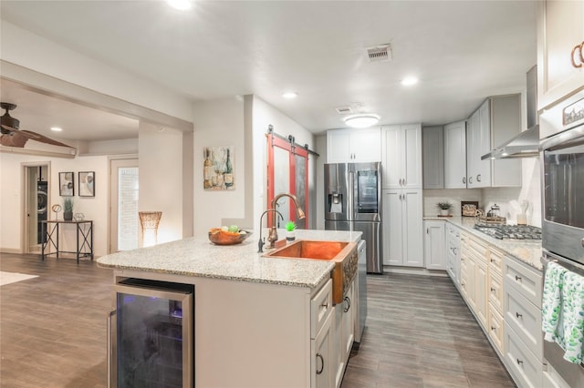 kitchen with visible vents, a center island with sink, beverage cooler, a barn door, and stainless steel appliances