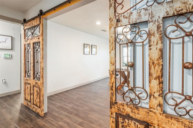 hallway with a barn door, baseboards, visible vents, and wood finished floors