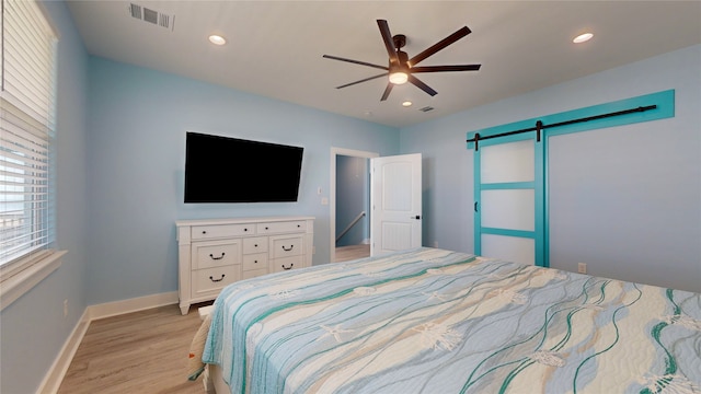 bedroom featuring light wood-type flooring, a barn door, and ceiling fan