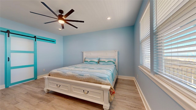 bedroom featuring ceiling fan, a barn door, and light hardwood / wood-style floors