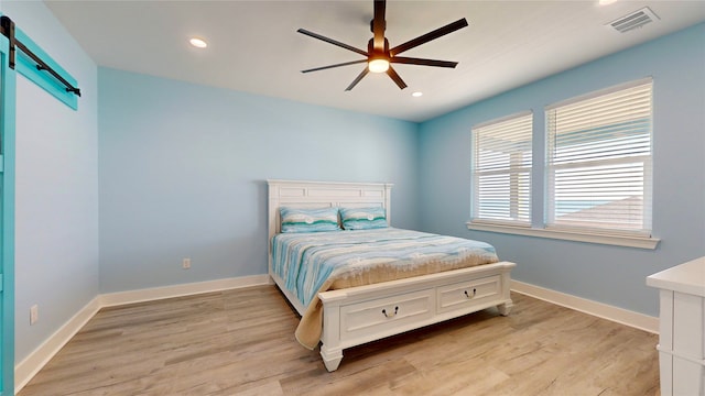 bedroom featuring a barn door, ceiling fan, and light hardwood / wood-style flooring