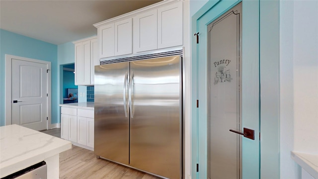 kitchen featuring white cabinets, light wood-type flooring, stainless steel refrigerator, and light stone counters