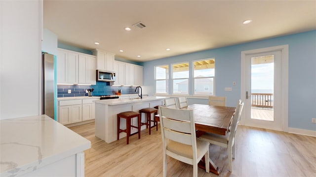 kitchen with decorative backsplash, light stone countertops, a kitchen bar, white cabinetry, and stainless steel refrigerator