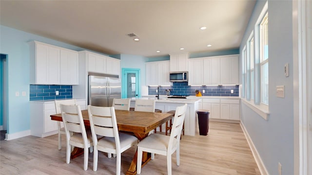 kitchen with white cabinets, backsplash, stainless steel appliances, and an island with sink