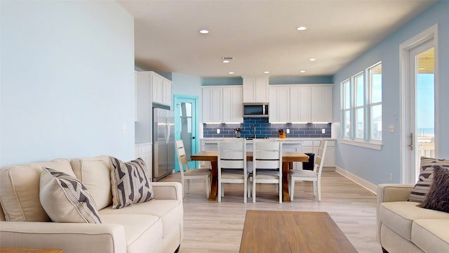 kitchen with decorative backsplash, light hardwood / wood-style flooring, white cabinets, and stainless steel appliances