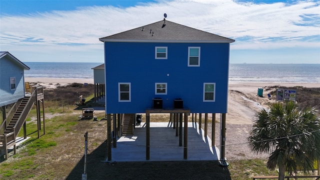 back of property with a water view, central AC unit, a beach view, and a carport