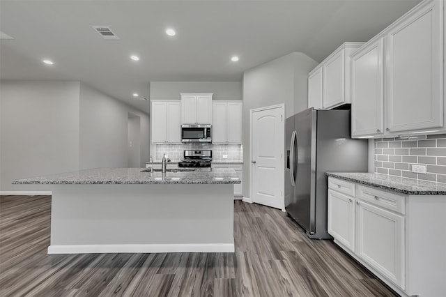 kitchen featuring light stone countertops, appliances with stainless steel finishes, tasteful backsplash, a kitchen island with sink, and white cabinets