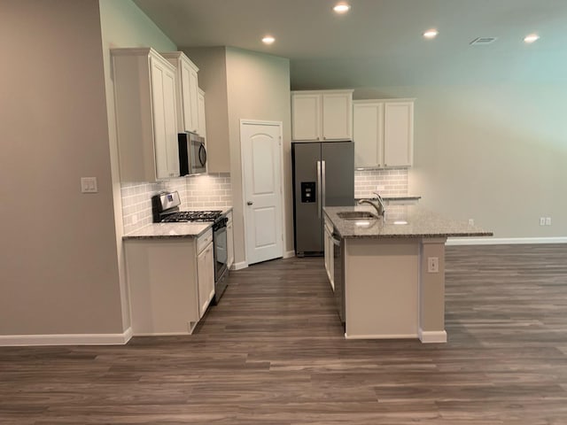 kitchen featuring dark wood-type flooring, a center island with sink, sink, light stone countertops, and appliances with stainless steel finishes