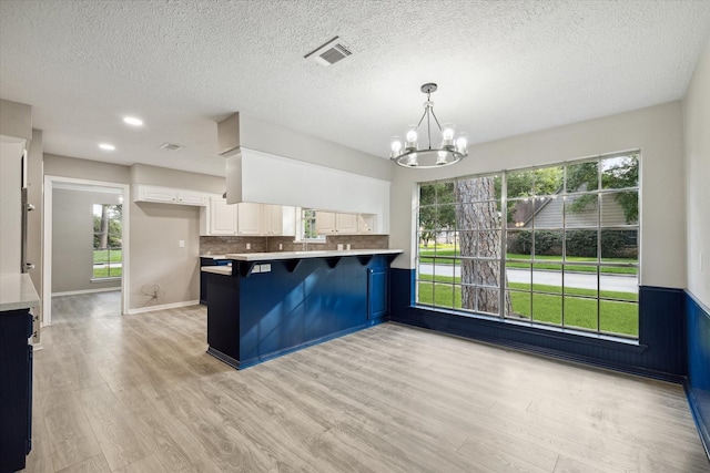 kitchen featuring a breakfast bar, backsplash, kitchen peninsula, a notable chandelier, and white cabinetry