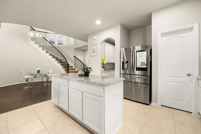 kitchen with white cabinetry, light stone countertops, a kitchen island, stainless steel fridge, and light tile patterned floors