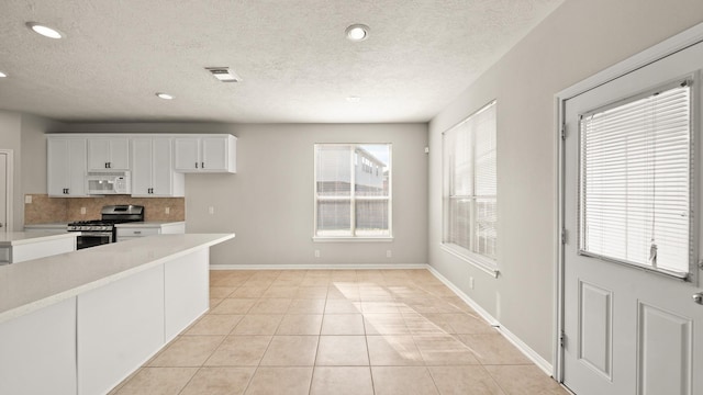 kitchen with stainless steel range with gas cooktop, decorative backsplash, light tile patterned floors, a textured ceiling, and white cabinetry