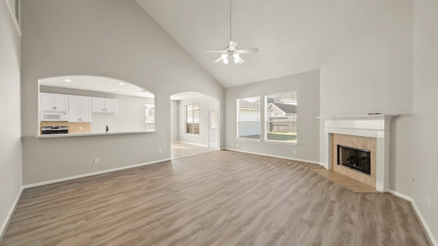 unfurnished living room with light hardwood / wood-style floors, high vaulted ceiling, ceiling fan, and a tiled fireplace