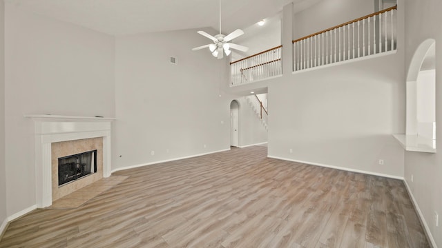 unfurnished living room with a tile fireplace, ceiling fan, high vaulted ceiling, and light hardwood / wood-style floors