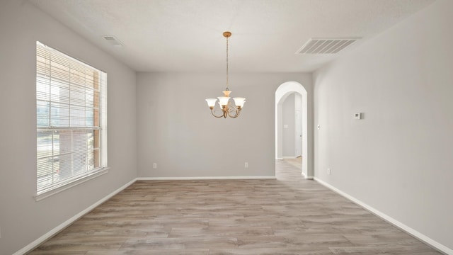 unfurnished dining area featuring plenty of natural light, light hardwood / wood-style floors, a textured ceiling, and an inviting chandelier