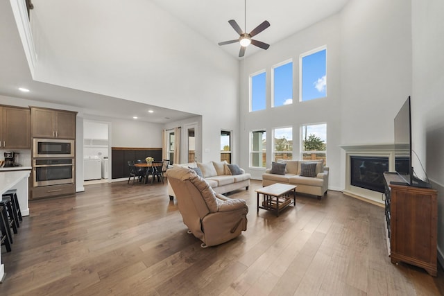 living room with a high ceiling, washer and clothes dryer, ceiling fan, and dark wood-type flooring