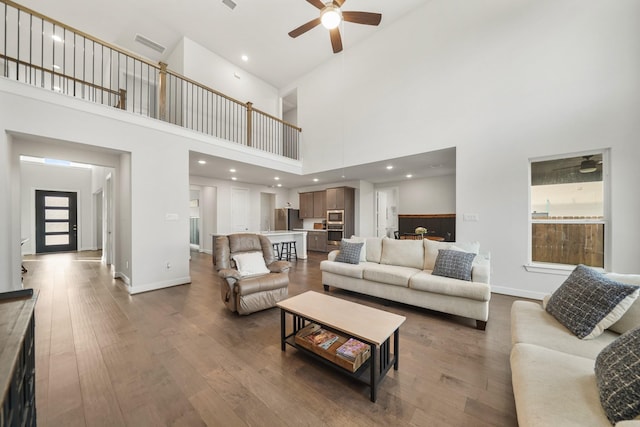 living room with a high ceiling, ceiling fan, and wood-type flooring