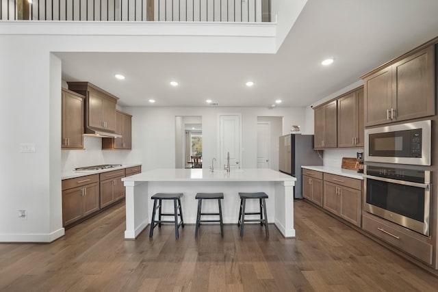 kitchen featuring dark hardwood / wood-style flooring, a center island with sink, appliances with stainless steel finishes, and a kitchen breakfast bar