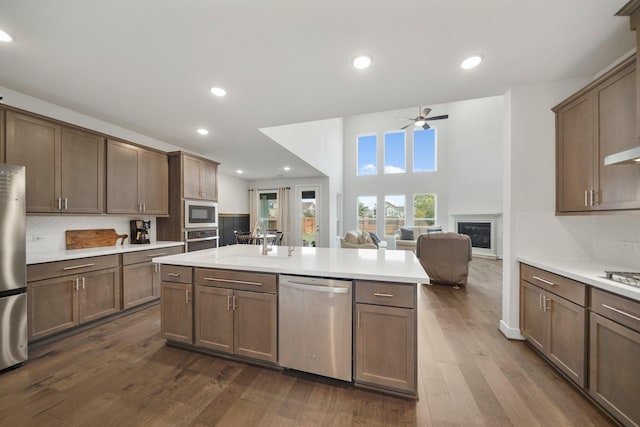 kitchen with a center island with sink, backsplash, dark hardwood / wood-style flooring, appliances with stainless steel finishes, and ceiling fan