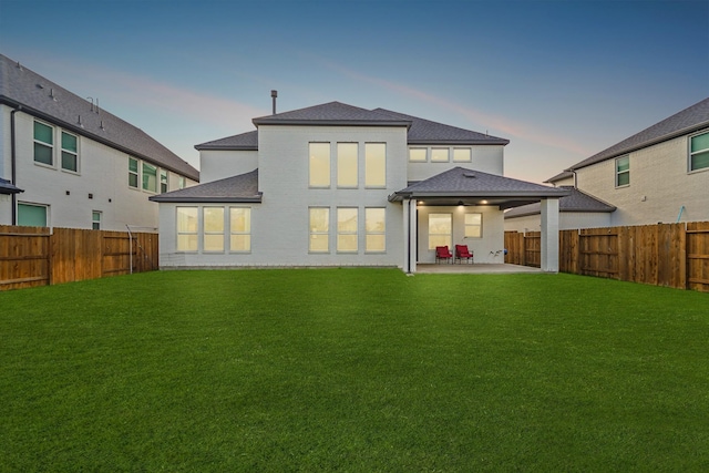 back house at dusk with a lawn, ceiling fan, and a patio