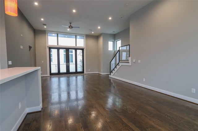 unfurnished living room featuring french doors, dark hardwood / wood-style flooring, ceiling fan, and a high ceiling