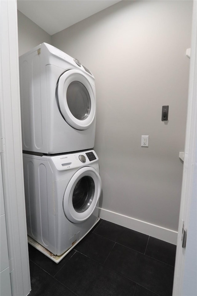 clothes washing area with dark tile patterned flooring and stacked washer and clothes dryer